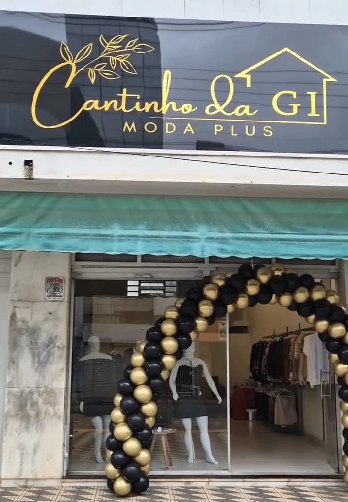 Fachada da loja Cantinho da Gi Moda Plus, com letreiro dourado e arco de balões pretos e dourados